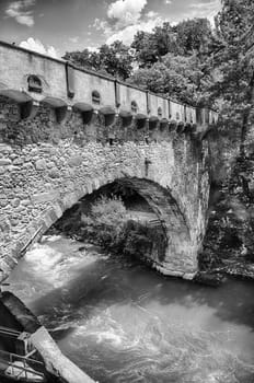 View of Steinerner Steg bridge crossing a river with lush green trees on both sides, iconic landmark in Merano, South Tyrol, Italy