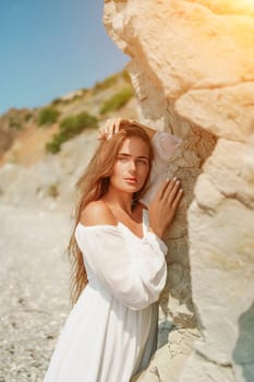 A woman in a white dress is standing on a rocky beach. Concept of serenity and tranquility, as the woman is enjoying the natural beauty of the beach