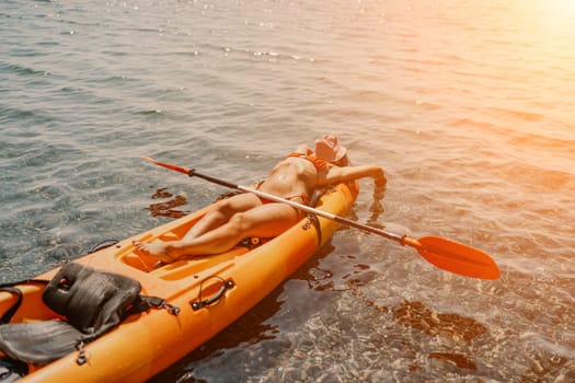 A woman is laying on a kayak in the water. The kayak is orange and has a paddle on it. The woman is wearing a red hat