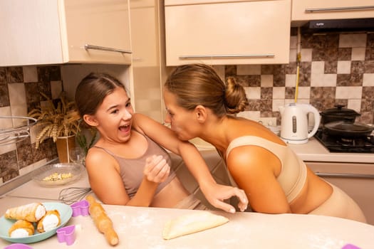 A woman and a girl are in a kitchen, laughing and playfully fighting while preparing food.