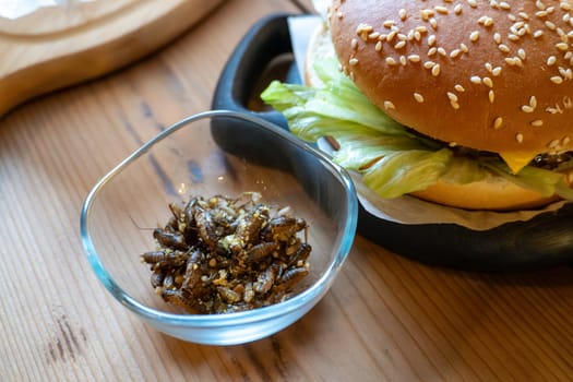 Gourmet burger with edible insects and fresh lettuce on wooden table.