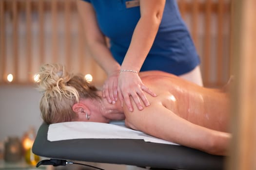 Relaxing Back Massage in a Spa Setting. A professional massage therapist in a blue uniform provides a relaxing back massage to a client lying on a massage table