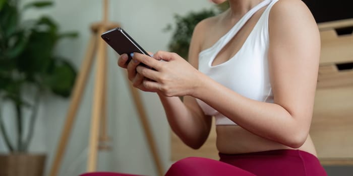 A fitness enthusiast practices yoga indoors, balancing technology and wellness. She focuses on her phone to follow along with a guided yoga session.
