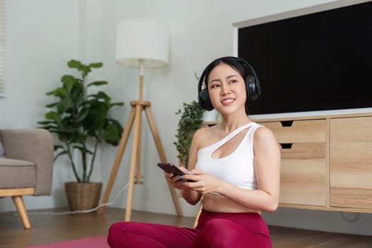 Embracing her fitness journey, a woman listens to music through headphones, combining her love for yoga and rhythm in an inviting home environment.