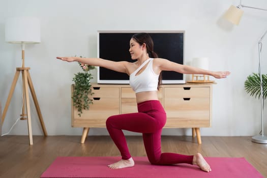 A woman is seen in a low lunge pose, emphasizing balance and stability in her yoga practice within her home atmosphere.