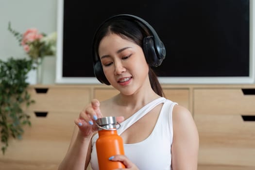 A woman enjoys her fitness routine while listening to music through headphones, ready to hydrate after an energetic workout.
