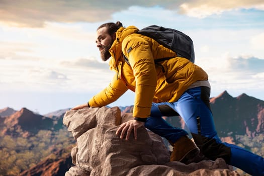 Determined traveler enjoys the solitude of a mountain summit, where the panoramic view represents adventure and personal growth. Hiker with outdoor gear feeling cold on the windy mountain top.