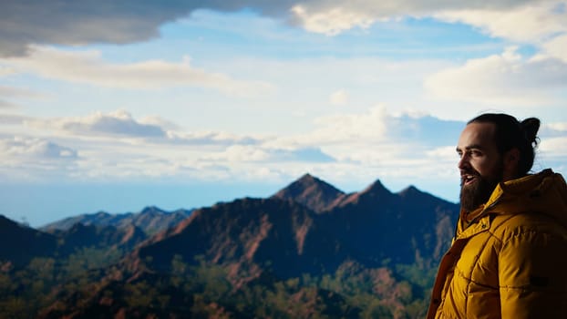 Thrilled traveler raises his arms in triumph after climbing the mountain top, enjoying the panoramic beauty of the nature. Feeling proud and admiring the vast sky and endless landscape. Camera A.