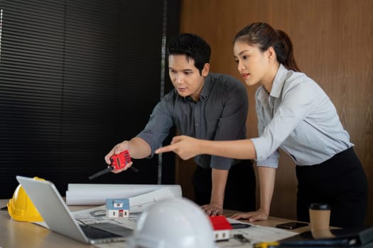 An engineer utilizes a measuring tool while discussing design ideas with a colleague, illustrating a critical step in project evaluation and execution.