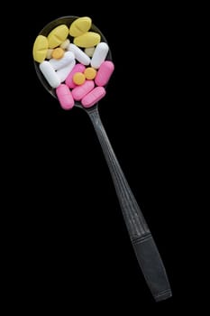 Top view of A lot of pills of different colors and shapes on Ancient vintage spoon isolated on Black background with clipping path. Concept of medication treatment and Health care, use it as your Space for text, Design, Wallpaper and Poster, Selective focus.
