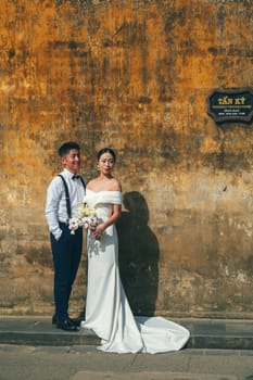 Vietnamese happy bride and groom. Beautiful Asian couple in love at a wedding ceremony on street in old town in Hoi An in Vietnam in Asia. Hoi An, Vietnam - December 1, 2024
