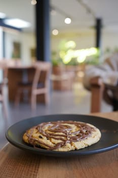 A warm cookie adorned with chocolate sits on a black plate in a cafe.