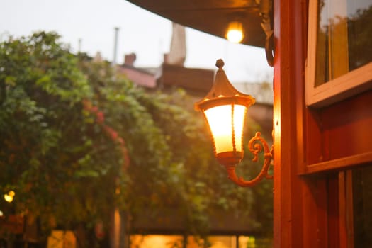 A warm light glows from a lamp beside a quaint building on a rainy day.