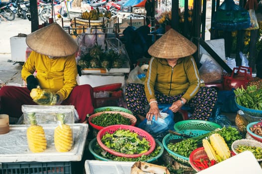 Asian street market with Vietnamese women selling fruits and vegetables on the street of old town in Hoi An city in Vietnam in Asia