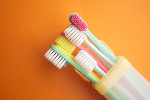 Vibrant toothbrushes in a clear holder on an orange backdrop.
