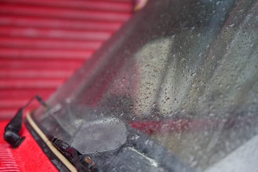 Water beads cover a car windshield as rain falls nearby in a vibrant setting.