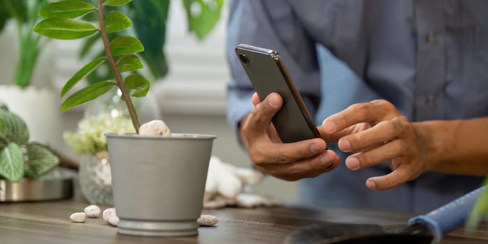 An individual interacts with their smartphone while tending to a potted plant, illustrating the integration of technology in traditional gardening.