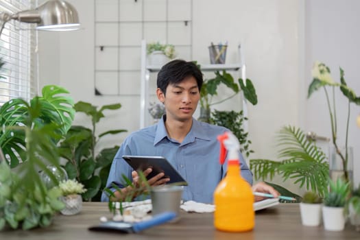 Engaged in sustainable gardening, a man utilizes his tablet to learn effective plant care methods while surrounded by vibrant indoor plants.