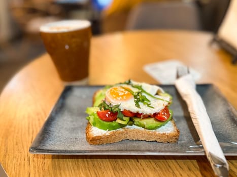 Avocado toast with egg served on a ceramic plate in cozy cafe. Healthy breakfast and balanced nutrition in a lifestyle setting