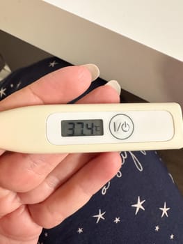 Digital thermometer showing body temperature in female hand during health check. Monitoring fever and early signs of illness at home