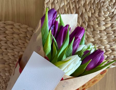 Purple and white tulip bouquet with greeting card on woven background. Seasonal floral gift and heartfelt personal message.