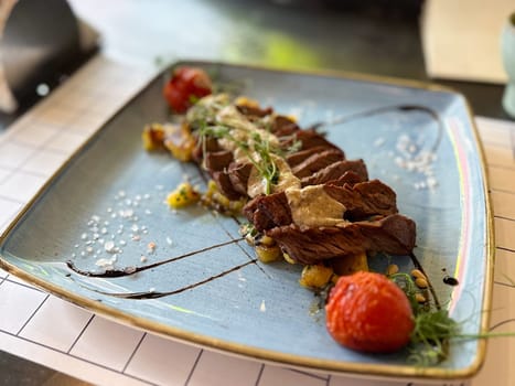Gourmet beef steak with sauce and vegetables on ceramic plate in restaurant setting. Modern cuisine, flavor, and elegant food presentation