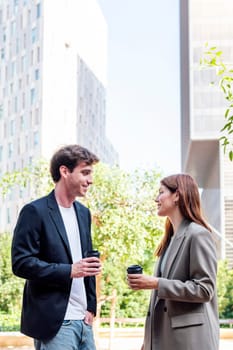 smiling man and a woman standing in a park near of office buildings talking while taking coffee, they are smiling and enjoying with the company, concept of business, copyspace for text