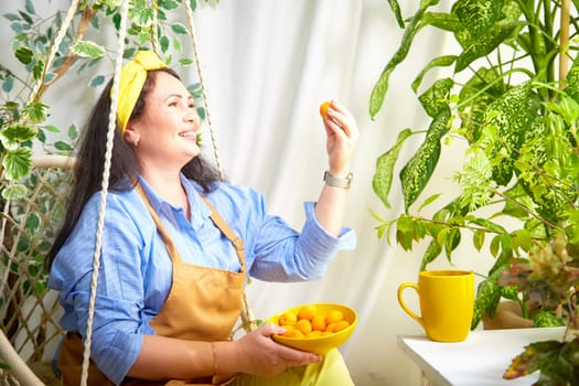 The gardener smiles as she holds a ripe fruit in her greenhouse, surrounded by vibrant plants.