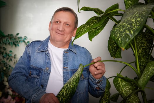 A middle-aged man smiles while holding a houseplant, posing cheerfully in a well-decorated indoor apartment space.