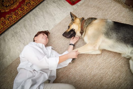 A woman in a cozy room smiles as she bonds with her German Shepherd dog during a relaxing moment.
