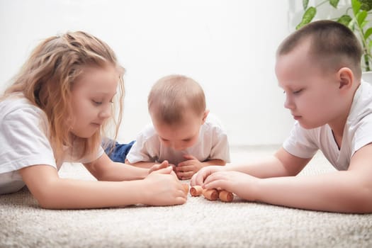 Three young children are focused on playing with small toys while lying on a cozy rug in a well-lit room.