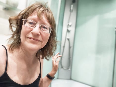 A middle-aged female blogger smiles for a morning selfie in the bathroom mirror, capturing her casual lifestyle moment.