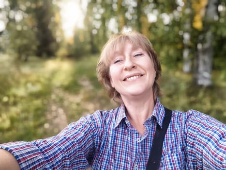 A middle-aged woman traveler captures a joyful selfie while exploring nature on a beautiful day in the forest.