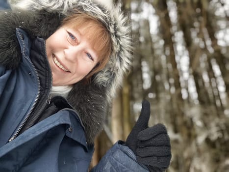 Mature tourist captures a joyful moment with a thumbs-up gesture in a snowy forest while exploring nature during her travel excursion.