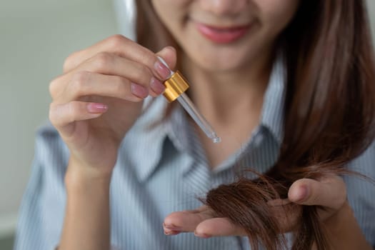 Focusing on her hair, a woman applies nourishing serum to promote vitality and shine, demonstrating the essential steps in haircare.