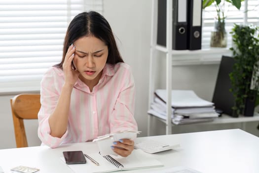 Struggling with financial pressure, a woman reflects on her bills in her home office, displaying the emotional weight of financial management.