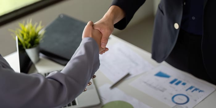 Two business professionals engage in a handshake, symbolizing agreement and collaboration, set against a backdrop of graphs and charts that represent success.