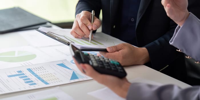 Two professionals engage in a detailed financial discussion, reviewing colorful graphs and notes while utilizing a calculator to enhance their analysis.