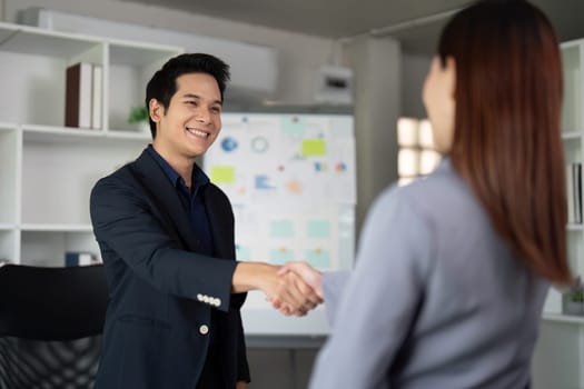 Two colleagues meet and shake hands in a contemporary workspace, symbolizing professionalism and collaboration in a corporate environment.