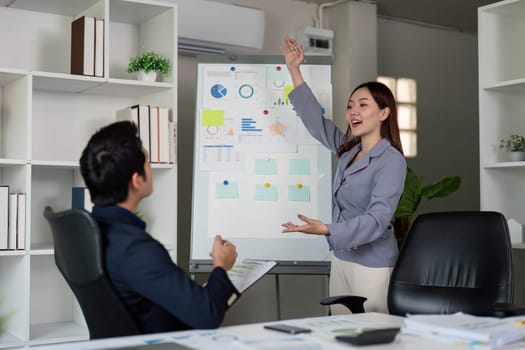 In a sleek office, a professional woman presents data and insights on a whiteboard, showcasing her communication skills and engaging her colleague in discussion.