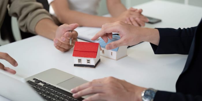 During a property consultation, a couple consults with their real estate agent, using a laptop and model homes to strategize their home buying decisions.