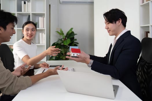 In a professional setting, a real estate agent shows models of houses to a couple, highlighting features while facilitating a fruitful discussion about their home buying needs.