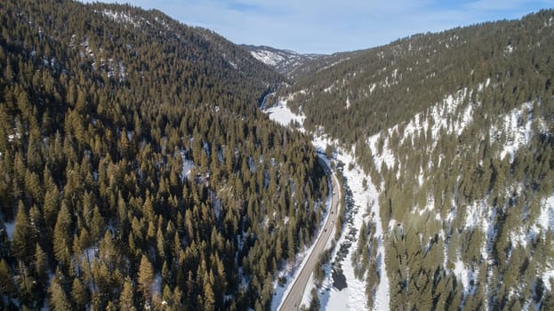 A snowy mountain range with a road running through it. The road is surrounded by trees and the sky is clear