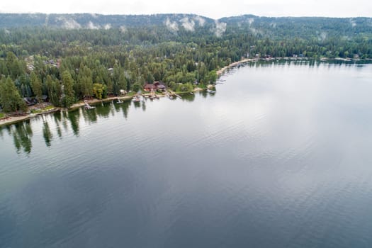 A lake with a forest in the background. The water is calm and clear. The sky is cloudy