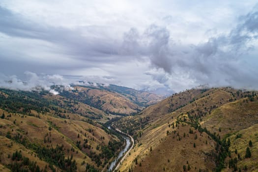 The sky is cloudy and the mountains are brown. The valley is filled with trees and the river is winding through it