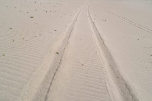 A sandy beach with a few footprints in the sand. The footprints are in a straight line, and the sand is very dry