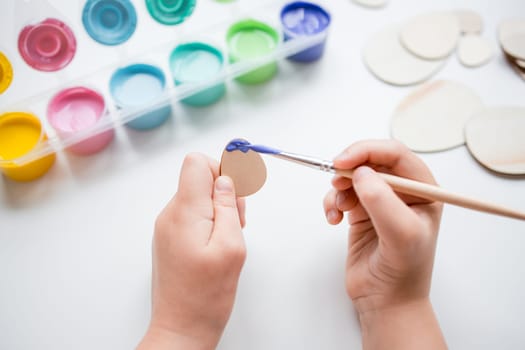 Child painting Easter wooden egg shapes with blue paint and brush.