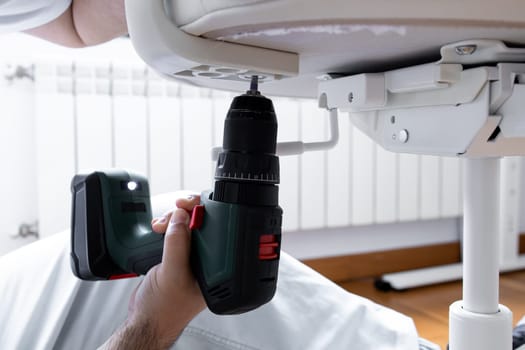 Male adult assembling furniture with electric drill indoors.