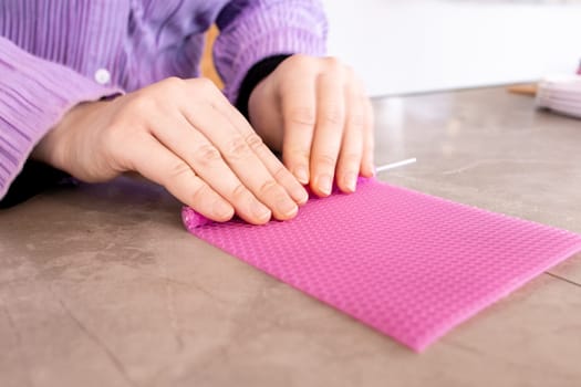 Hands crafting pink beeswax candle on marble surface.