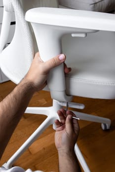 Male assembling white office chair with allen wrench on wooden floor.